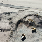 Aerial view of excavators and yellow dump trucks working in an open-pit mine in arid desert terrain