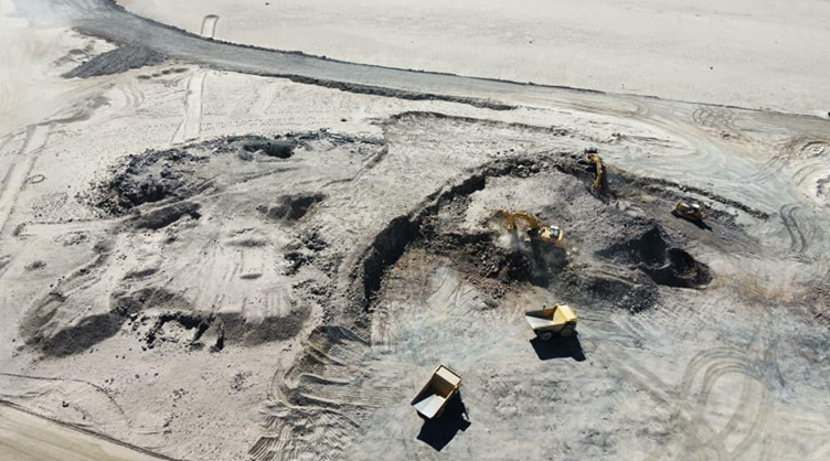 Aerial view of excavators and yellow dump trucks working in an open-pit mine in arid desert terrain