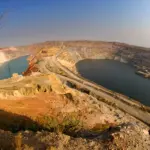 Aerial view of a large terraced open-pit mine with water-filled sections and a haul road along a central ridge