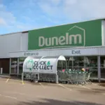 Dunelm store entrance with a large green Dunelm sign and a Click & Collect trolley shelter in the car park