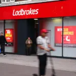 Red Ladbrokes betting shop frontage with pedestrians passing on the pavement outside