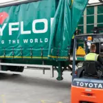 Forklift loading pallets onto a green Polyflor-branded lorry trailer marked 'Covering the World'