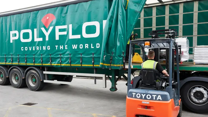Forklift loading pallets onto a green Polyflor-branded lorry trailer marked 'Covering the World'