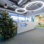 Reception area of a modern office with an illuminated BCG Baltic Classifieds Group sign, a decorated Christmas tree and a glass meeting room.
