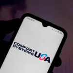 Hand holding a smartphone displaying the Comfort Systems USA logo against a blurred purple background.