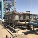 Row of large filter vessels and blue process pipes at an industrial oil and gas water treatment facility under a clear sky