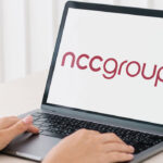 Person typing on a laptop whose screen shows the NCC Group logo