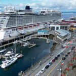 Aerial view of the Norwegian Bliss cruise ship docked at a waterfront pier beside a marina and city street