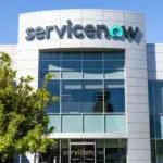 ServiceNow logo on the facade of a modern glass and white office building under a blue sky.