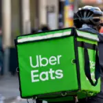 Delivery courier in a helmet carrying a green Uber Eats backpack along a city street