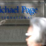 Blue Michael Page International sign on a glass panel mounted to a stone wall, with blurred passers-by in the foreground