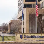 UnitedHealthcare corporate office building with a stone entrance sign displaying the UnitedHealthcare name and logo, and flags flying in front.