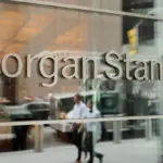 Morgan Stanley name in metal letters on a glass office building facade, with pedestrians reflected below