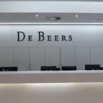 Reception area with a white wall displaying the De Beers name in dark lettering above a long white counter.