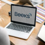 Laptop on a desk displaying the Beeks logo, with a woman working in the foreground
