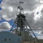 Steel mine headframe flying a Cornish flag above a blue industrial building under a cloudy sky
