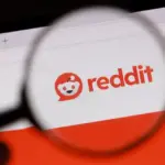Magnifying glass held over a computer screen showing the Reddit logo