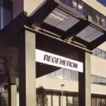 Entrance to a Regeneron office building with an illuminated "REGENERON" sign under a dark canopy against a blue sky