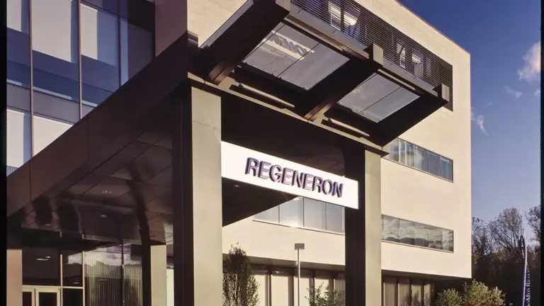 Entrance to a Regeneron office building with an illuminated "REGENERON" sign under a dark canopy against a blue sky