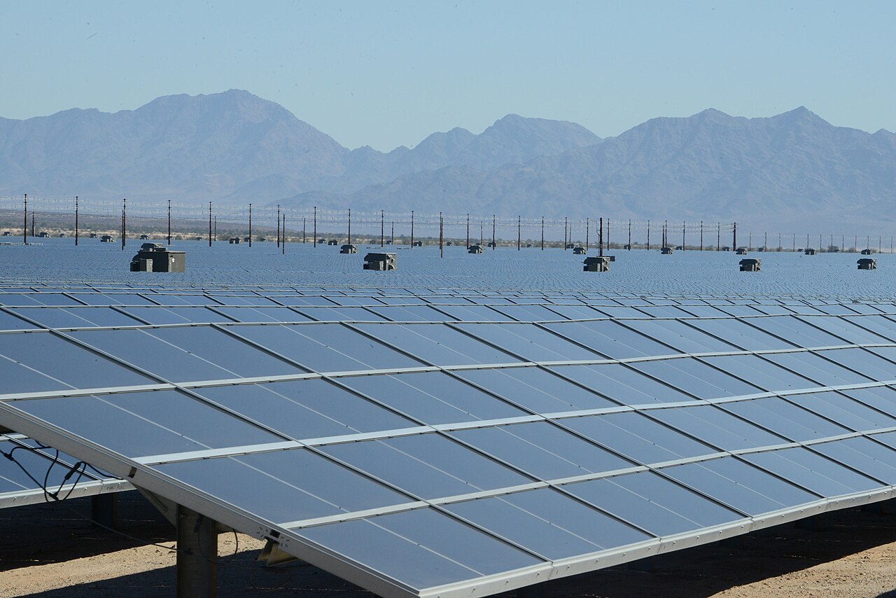 Rows of solar panels stretching across a desert solar farm with dry mountains in the background