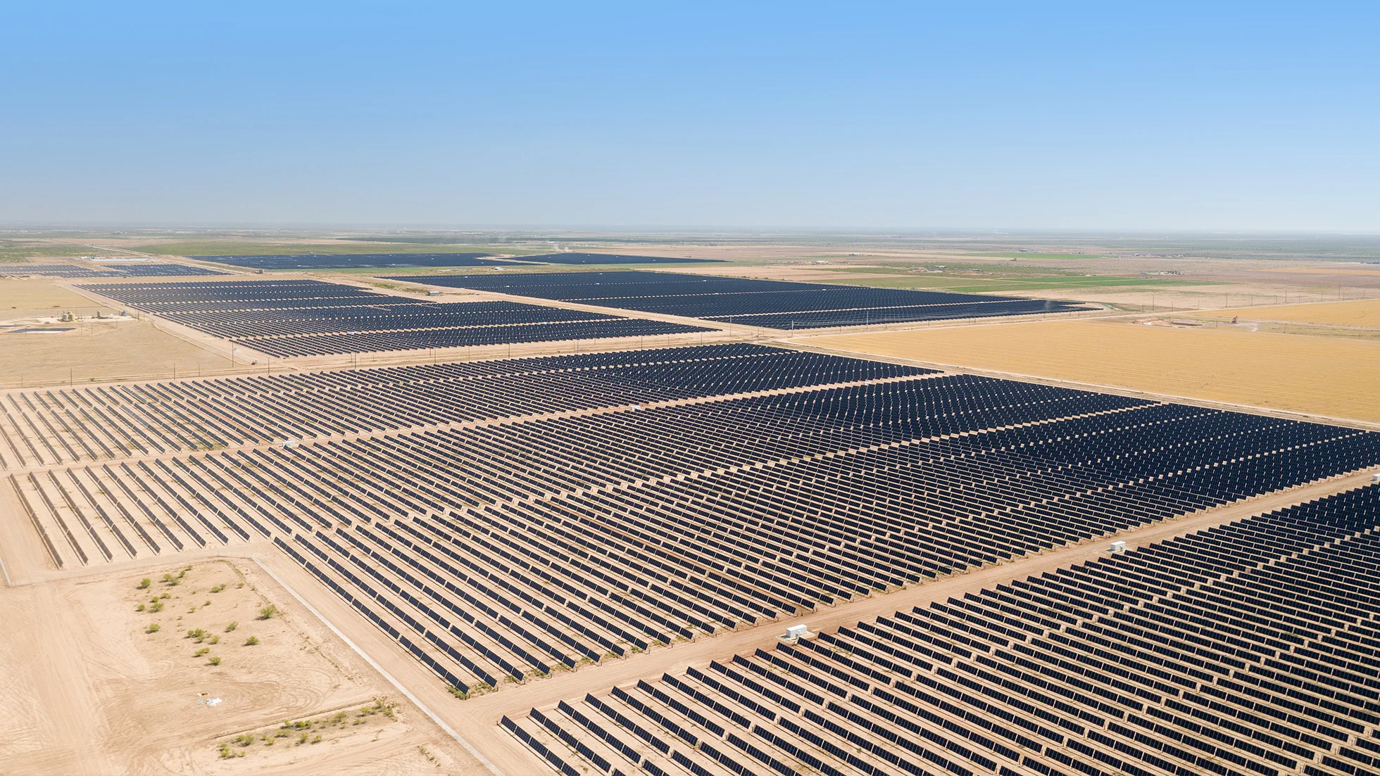 Aerial view of a large utility-scale solar farm with long parallel rows of solar panels across flat desert terrain